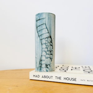 Puede incluir: Un jarrón cilíndrico de cerámica azul claro con un diseño texturizado en un lado. El jarrón está sobre un libro titulado "MAD ABOUT THE HOUSE" de Kate Watson.