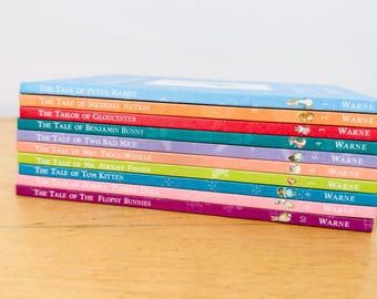 May include: A stack of ten colorful children's books by Beatrix Potter, each with a distinct spine color including light blue, orange, red, teal, purple, light pink, lime green, blue, pink, and dark purple, all featuring the Warne logo.