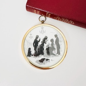 Op de afbeelding: Een ronde, goudomrande silhouetkunst die een scène uit het Victoriaanse tijdperk toont met figuren in kleding uit die periode. De zwart-wit afbeelding toont verschillende mensen, waaronder een vrouw met een waaier, een man in een pak en een kleine hond. Een rood boek is zichtbaar op de achtergrond.