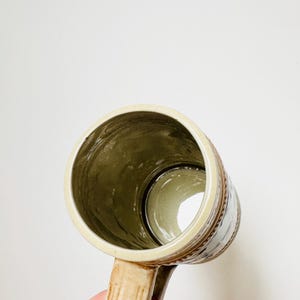 Op de afbeelding: Een keramische bierkan met een bruin en wit ontwerp. De kan heeft een handvat en is gemaakt van lichtbruine keramiek.