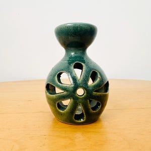 Peut inclure: Un diffuseur d'huiles essentielles en céramique vert d'eau avec un motif en forme de fleur. Le diffuseur a une base ronde avec des formes de pétales découpées et un dessus cylindrique. La céramique a une finition brillante.