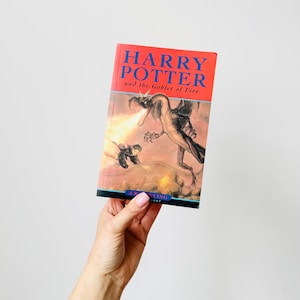 May include: A hardcover book titled "Harry Potter and the Goblet of Fire" with a red cover. The cover art depicts a dragon breathing fire at a figure. The author's name, J.K. Rowling, is at the bottom.