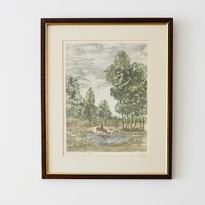 May include: A framed landscape print featuring a watercolour-style scene of deer drinking from a small pond surrounded by green trees and a cloudy sky. The artwork is encased in a dark brown wood frame with a gold inner trim and a cream-coloured mat.