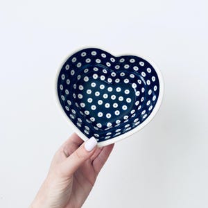 Puede incluir: Un cuenco de cerámica en forma de corazón con un esmalte azul marino profundo decorado con un patrón repetitivo de pequeños puntos blancos con centros oscuros. El interior del cuenco muestra el mismo motivo de puntos y el borde es blanco.
