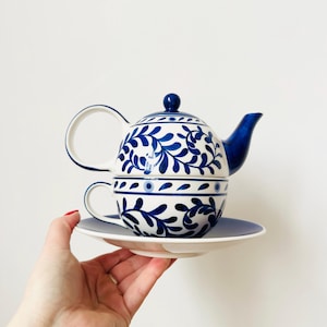 Peut inclure: Service à thé en céramique blanc et bleu avec un motif floral. L'ensemble comprend une théière, une tasse et une soucoupe. La théière a une anse incurvée et un couvercle avec un petit bouton. La tasse et la soucoupe sont empilées. Motif bleu et blanc classique.