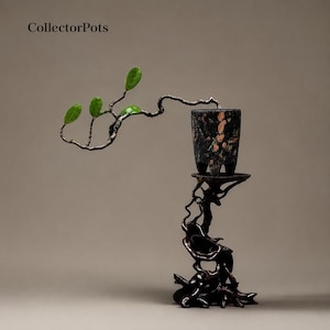 May include: A dark, mottled stone pot with three feet sits atop a tall, intricate, dark brown wooden stand. A thin, winding branch with small, vibrant green leaves extends horizontally from the pot. The text CollectorPots appears in the top left.