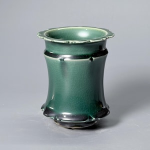 Pode incluir: Um vaso de cerâmica cilíndrico com um esmalte verde-floresta profundo e um padrão de fissuras visível. O recipiente tem uma borda alargada e recortada com uma base a condizer, e um corpo ligeiramente côncavo que se estreita para o centro.