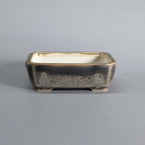 May include: A rectangular ceramic bonsai pot with a textured, mottled black and dark gray exterior finish. The interior of the vessel is glazed in a smooth, off-white color. The pot features four small, integrated feet at the base corners.