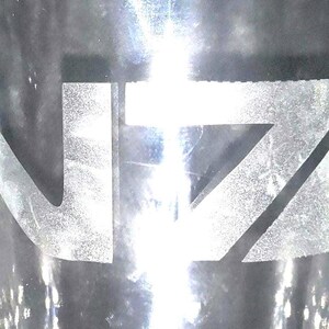 May include: A clear glass with the letters "NZ" etched on the front in white.