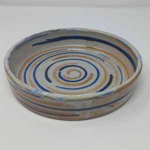 May include: A ceramic bowl with a spiral pattern. The bowl has concentric circles in blue and tan on a speckled, off-white base. The rim has a dark blue accent. The bowl is about 5 cm tall and 20 cm in diameter.