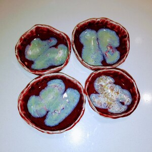 May include: Four small, red ceramic bowls with a white and green glaze. The bowls have a slightly irregular shape and a textured rim.