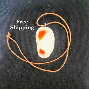 Puede incluir: Un colgante blanco con inclusiones de ágata naranja y roja, colgado de un cordón de cuero marrón.