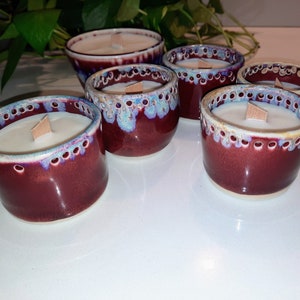 Puede incluir: Seis portavelas de cerámica color burdeos con detalles en blanco y azul. Cada portavelas tiene una vela blanca con una mecha de madera.