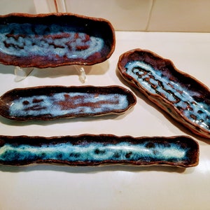 May include: Four ceramic dishes with a blue and brown glaze. The dishes are long and narrow, and they have a slightly wavy edge. They are perfect for serving small snacks or appetizers.