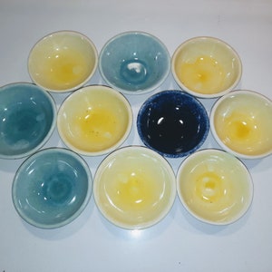 May include: A set of ten small ceramic bowls in various shades of blue and yellow. The bowls are all round and have a slightly raised rim.