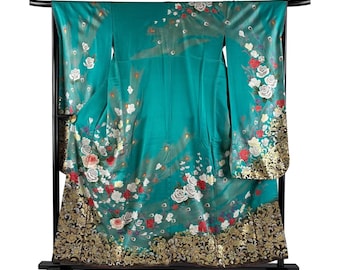 May include: A teal kimono with a floral pattern of white and red roses, displayed on a black stand. The bottom hem features a gold and black ornate design. The kimono is made of a silky material.