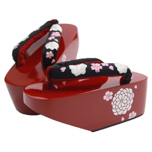 May include: A pair of traditional Japanese geta sandals. The wooden platform sandals are a glossy red with a black fabric thong adorned with white and pink floral embroidery. Floral designs are also painted on the sides.