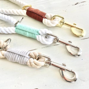 May include: Three dog leads with white rope and colourful suede accents. The leads have a brown, mint green, and grey suede wrap near the clasp. Each lead has a metal clasp and ring for easy attachment to a dog collar.