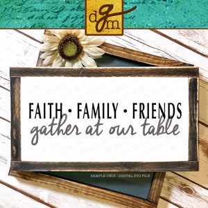 May include: A white wooden sign with a black frame and the text "FAITH FAMILY FRIENDS gather at our table". The sign is on a white wooden surface with a sunflower in the background.
