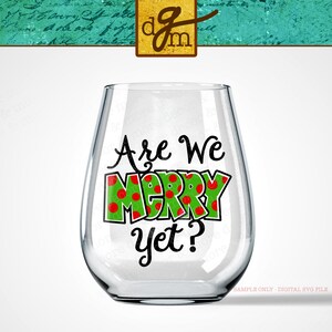 May include: A clear glass wine glass with a green and red design that says "Are We Merry Yet?" on it.
