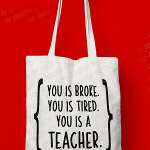 May include: White tote bag with black text that reads "You is broke. You is tired. You is a teacher."
