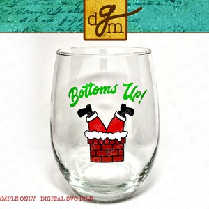 Może przedstawiać: Przezroczysty kieliszek do wina bez n&oacute;żki z zielonym napisem "Bottoms Up!". Poniżej tekstu znajduje się grafika n&oacute;g i st&oacute;p Świętego Mikołaja wystających z komina. Komin jest z czerwonej cegły z białym obramowaniem.