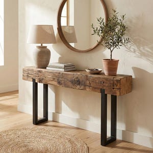 May include: A rustic wooden console table with black metal legs. A beige lamp, books, and a small potted plant sit on the table. A round mirror hangs on the wall above the table, and a woven rug is on the floor.