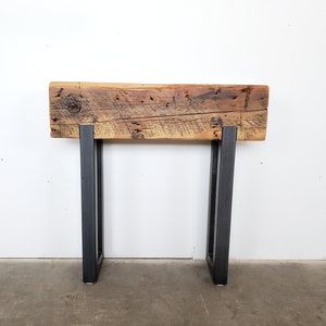 May include: A rustic wooden console table with a reclaimed wood top and black metal legs. The table is approximately 30 inches wide and 16 inches tall.