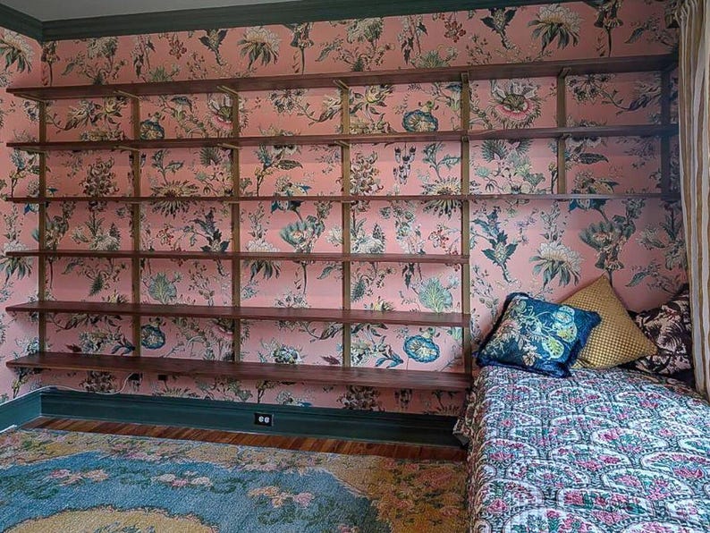 Wall mounted bookcase in a whimsical room featuring black walnut solid hardwood shelves and heavy duty brass finish steel brackets.