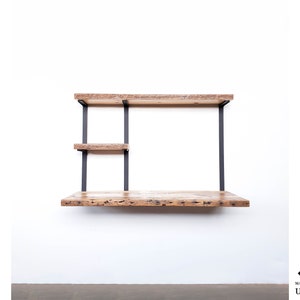 Puede incluir: Un escritorio de pared con una tapa de madera r&uacute;stica y soportes de metal negro. El escritorio tiene dos estantes para almacenamiento.