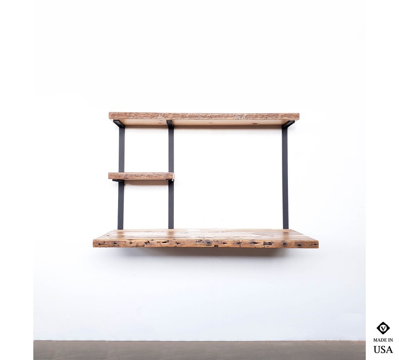Puede incluir: Un escritorio de pared con una tapa de madera r&uacute;stica y soportes de metal negro. El escritorio tiene dos estantes para almacenamiento.