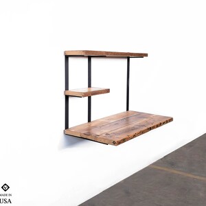 Puede incluir: Un escritorio de pared con dos estantes hechos de madera recuperada y soportes de metal negro. El escritorio mide aproximadamente 76 cm de ancho y 46 cm de profundidad. Los estantes miden aproximadamente 25 cm de ancho y 15 cm de profundidad. El escritorio est&aacute; hecho en los Estados Unidos.