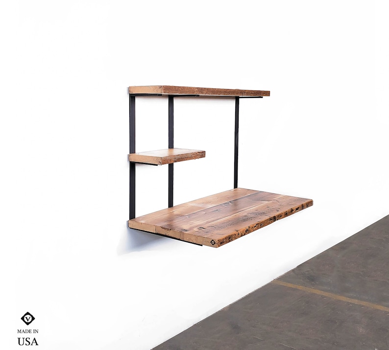 Puede incluir: Un escritorio de pared con dos estantes hechos de madera recuperada y soportes de metal negro. El escritorio mide aproximadamente 76 cm de ancho y 46 cm de profundidad. Los estantes miden aproximadamente 25 cm de ancho y 15 cm de profundidad. El escritorio est&aacute; hecho en los Estados Unidos.