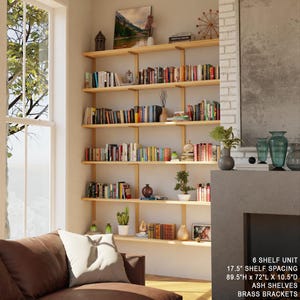tall bookshelf with solid wood shelves and metal brackets with brass finish. 6 shelves tall bookcase in tall ceiling livingroom next to window.