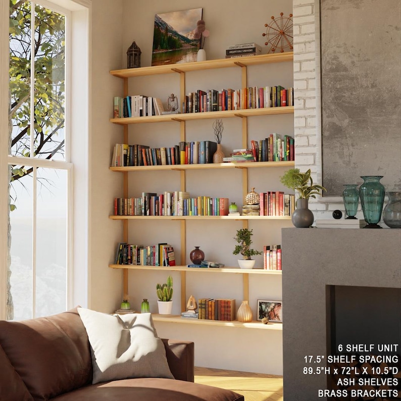 tall bookshelf with solid wood shelves and metal brackets with brass finish. 6 shelves tall bookcase in tall ceiling livingroom next to window.