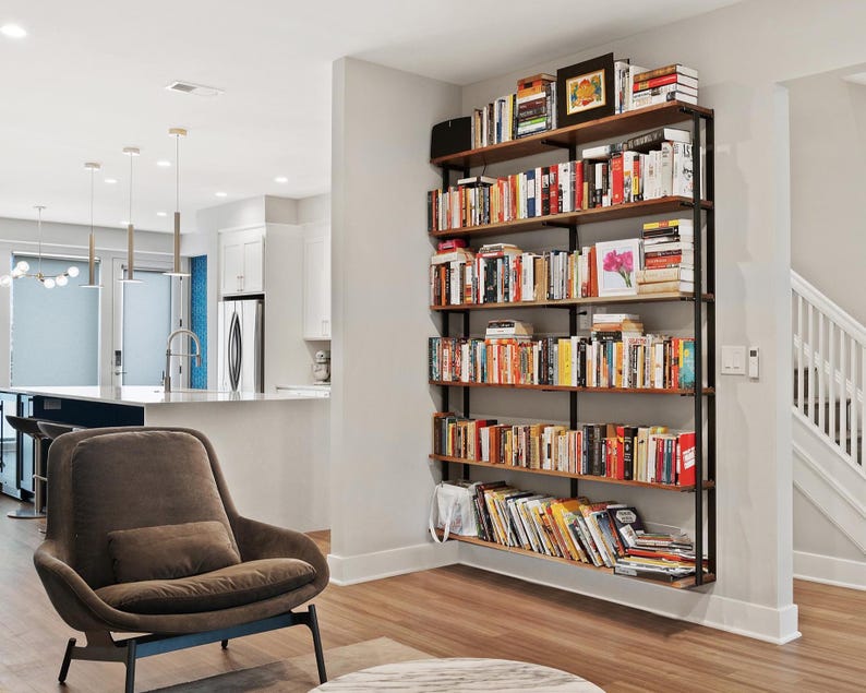 Modern industrial wall mounted bookcase. 6-tier shelving unit with black walnut wood and steel brackets filled with books in living room