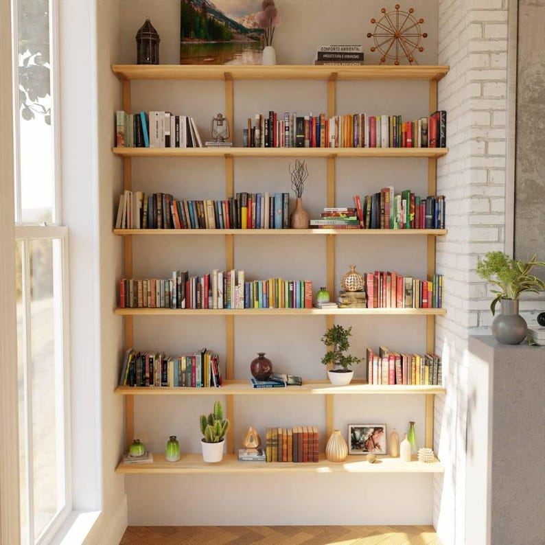 Sleek 6 shelf solid ash wood floating bookshelf supported by heavy duty brass finish American steel brackets in a cozy living mid-century modern living room.