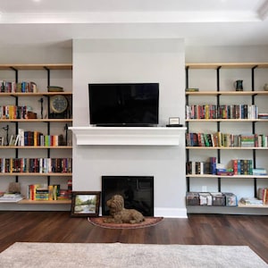Tall wall mounted bookshelves on both sides of a fireplace. Solid ash wood shelves with black brackets.