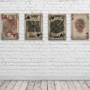 May include: Four vintage playing cards, Queen, King, Jack, and Ace of Spades, are displayed on a white brick wall. The cards are printed with a distressed, antique look.