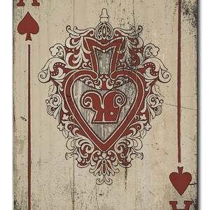 May include: A vintage-style playing card with a red and white design. The card is the Ace of Spades and features a stylized heart with a spade in the center. The card is on a wood background.