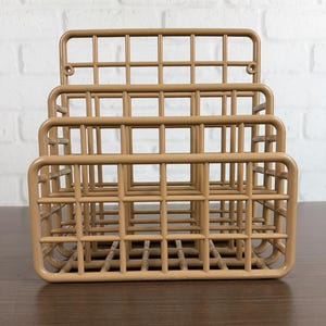 May include: A tan-colored, three-tiered desk organizer with a grid-like design. The organizer is made of metal and has a rectangular shape. The design is open, allowing for easy viewing of the contents. The organizer is suitable for storing documents, letters, or office supplies.