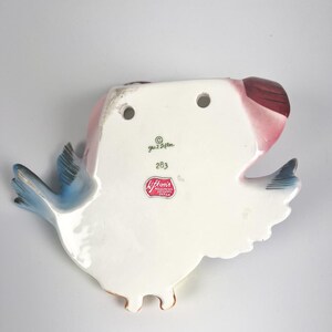 May include: A white ceramic wall pocket shaped like a bird with blue wings and a red tail. The back features two holes for hanging, the text Geo. Z. Lefton, the number 283, and a red sticker label that reads Lefton's Reg. U.S. Pat. Off. Made in Japan.