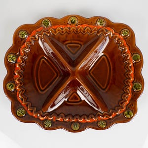 May include: A brown ceramic serving dish with four compartments. The dish has a scalloped edge with orange and zig-zag detailing. Green and yellow circular accents are spaced around the rim. The dish is designed for serving snacks or appetizers.