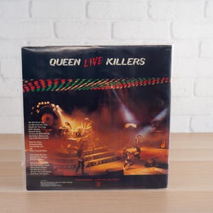 May include: A vintage vinyl record album titled "Queen Live Killers." The album cover features a live concert scene with the band performing on stage. The album's tracklist is visible on the left side of the cover.