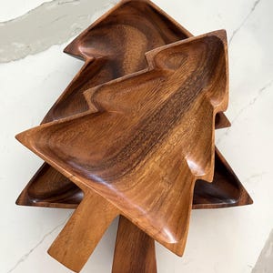 May include: Two wooden tree-shaped serving trays. The trays are made of a dark brown wood with visible grain. The trays are stacked on top of each other, with the top tray slightly angled. The trays have a smooth, polished finish.