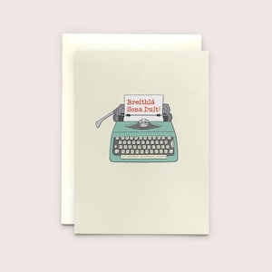 May include: Greeting card with a teal vintage typewriter illustration. The paper in the typewriter reads "Breithlá Sona Duit!" in red text. The card is on a cream background with a matching envelope.