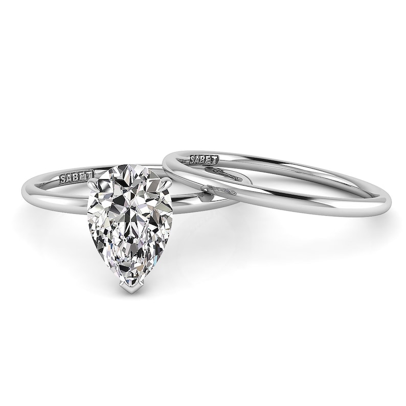 Puede incluir: Un anillo de compromiso de diamante de forma pera engastado en oro blanco con una banda de boda a juego. El anillo est&aacute; grabado con la palabra "SABET" en la banda.