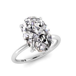 May include: A solitaire engagement ring with a large, oval-cut diamond. The diamond is set in a four-prong setting on a thin, polished silver band. The band is stamped with "14K".