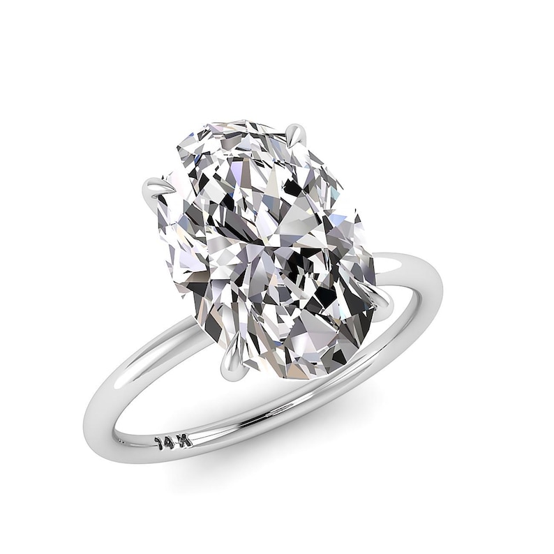 May include: A solitaire engagement ring with a large, oval-cut diamond. The diamond is set in a four-prong setting on a thin, polished silver band. The band is stamped with "14K".
