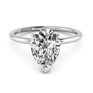 Puede incluir: Un anillo de compromiso de plata con un diamante de forma de pera. El anillo est&aacute; grabado con la palabra "SABET".